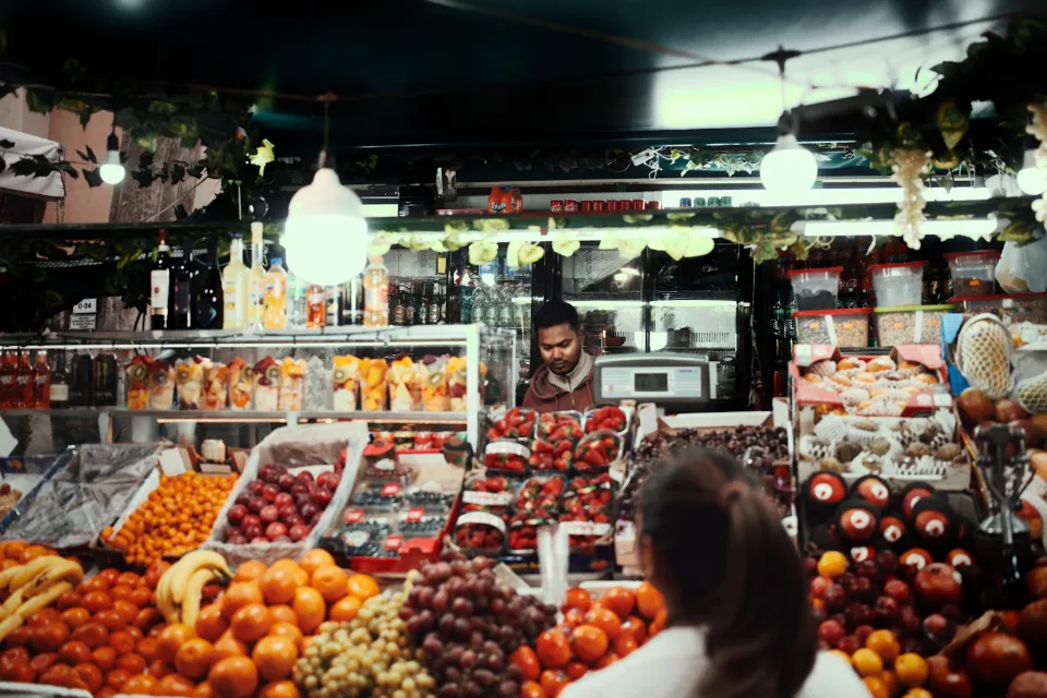 A greengrocer serving a customer across a counter of fruit