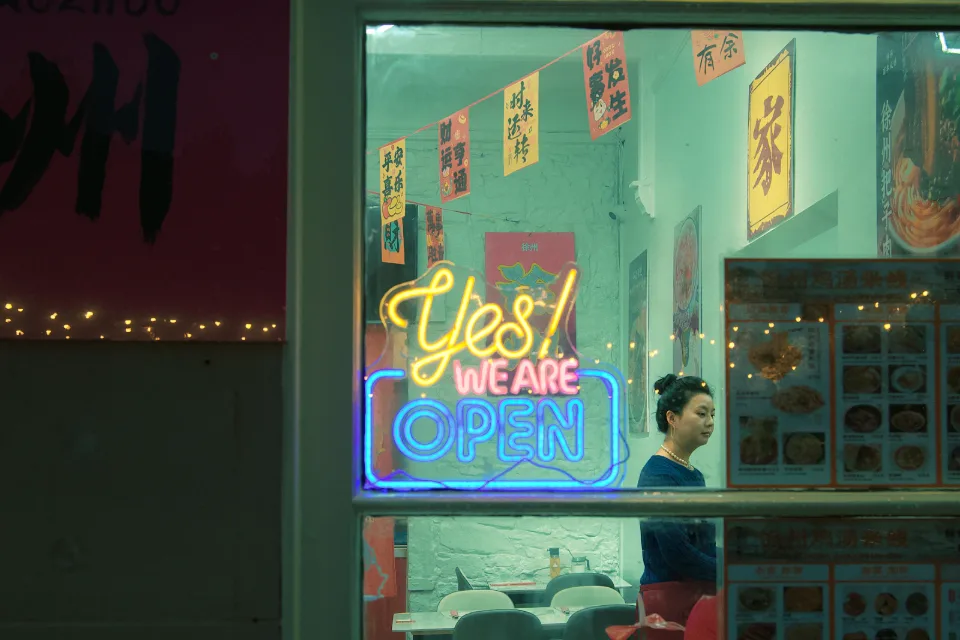 A lit window at night with a neon sign reading Yes! We are open