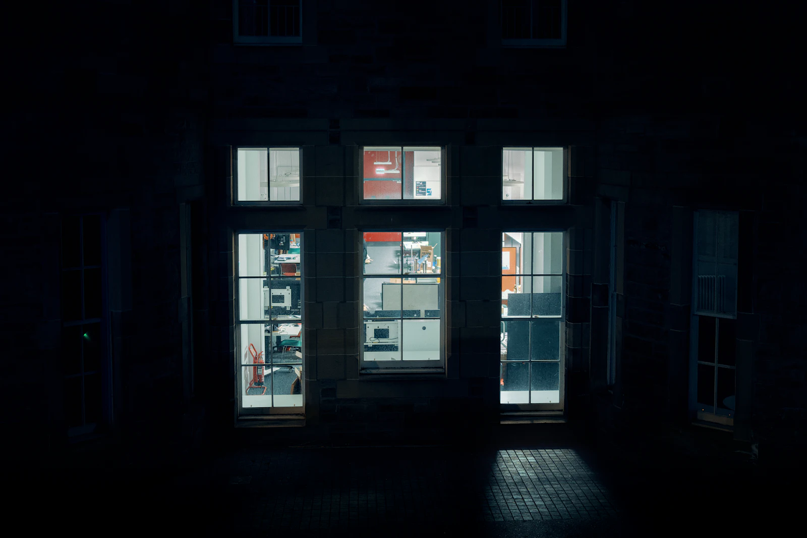 Three tall windows lit late at night in a dark stone building
